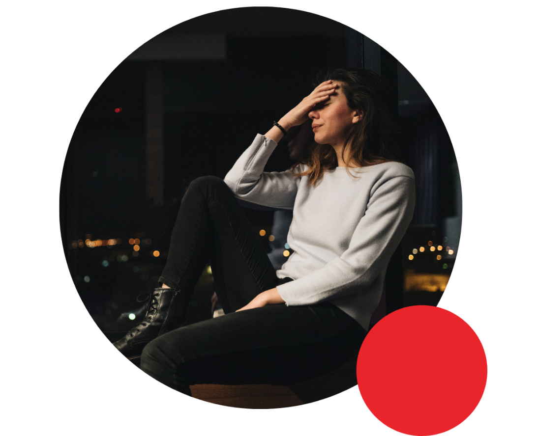 A woman sits by a city window at night, holding her head, weighed down by unresolved childhood trauma